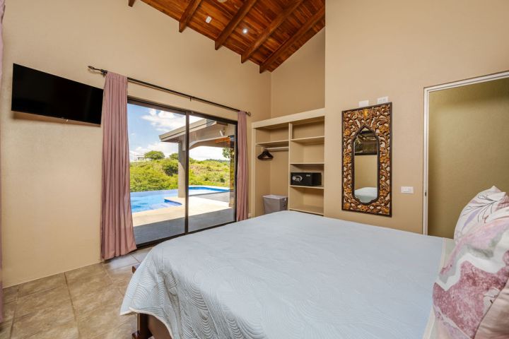 Bedroom with pool view, mirror, shelves, TV, and bed with light blue cover.