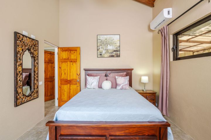 Cozy bedroom with wooden bed, decorative mirror, wall art, lamp, and window.