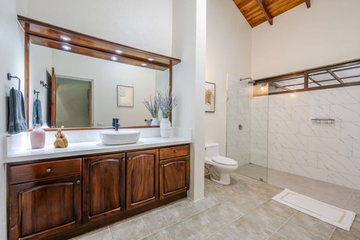 Bathroom with wooden vanity, marble shower, toilet, and large mirror.