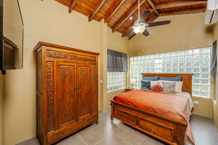Bedroom with wooden furniture, orange bedspread, ceiling fan, and glass block windows.