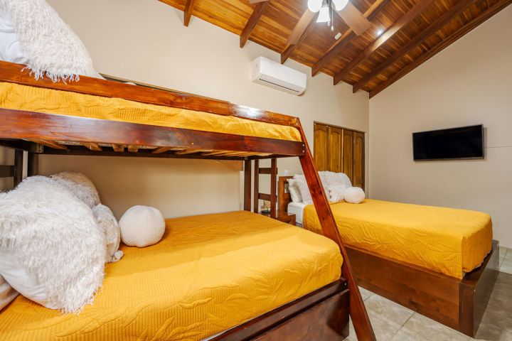 Room with wooden bunk beds and yellow bedding, ceiling fan, TV, and air conditioning unit.