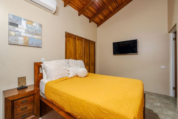 Bedroom with yellow bedding, wood accents, wall art, and wall-mounted TV.