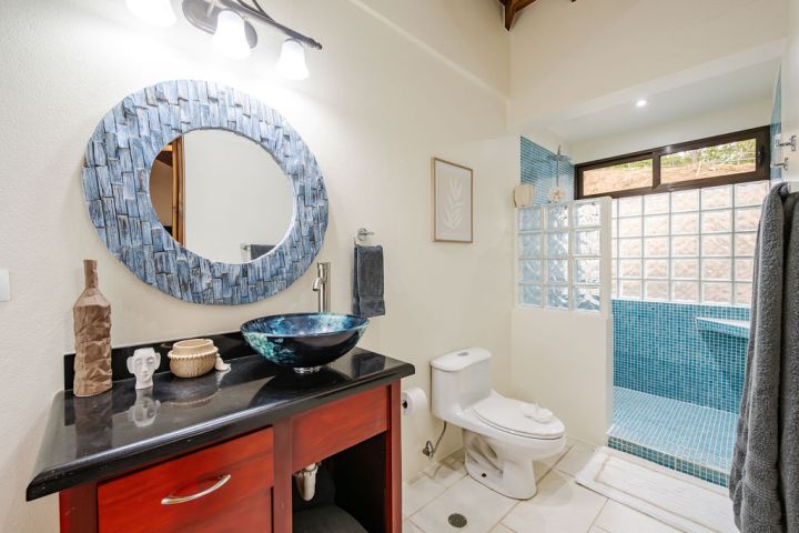 Modern bathroom with round mirror, blue sink, glass shower, and wood vanity.