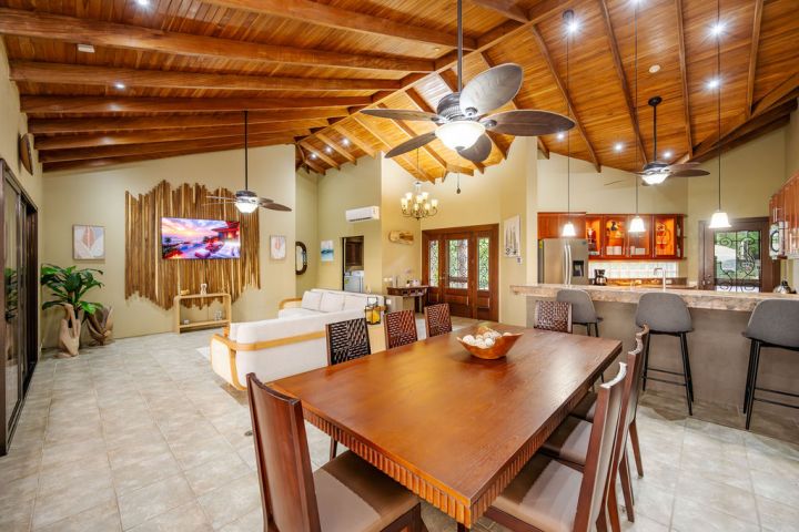 Spacious open-plan living area with wooden ceiling, dining table, kitchen, and cozy seating.