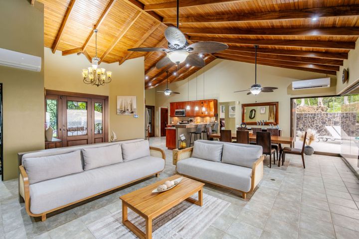 Spacious living room with wooden ceiling, sofas, dining area, and open kitchen.
