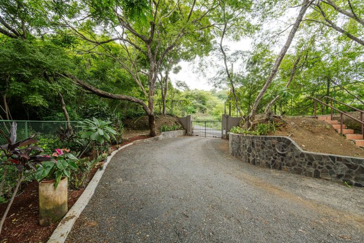 Gravel path leading to a gated entrance surrounded by lush green trees and shrubs.
