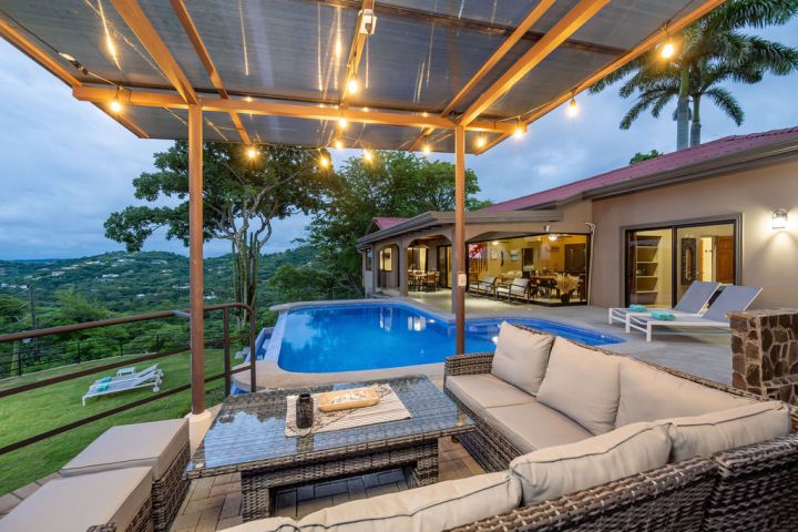 Outdoor patio with pool, lounge area, and lights overlooking a scenic view.