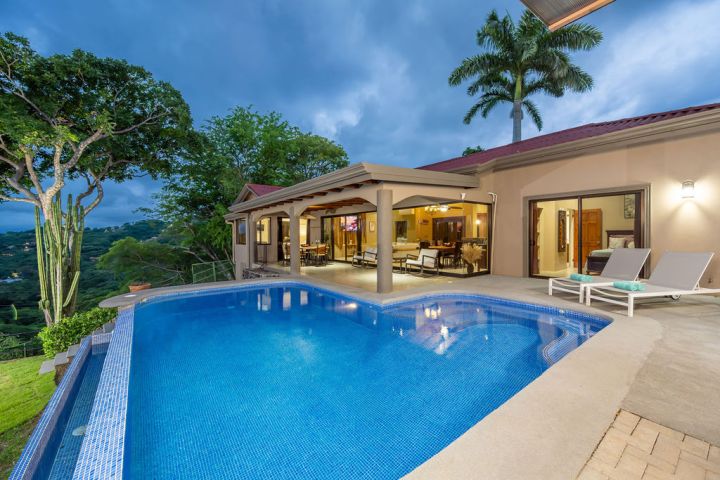 Luxury house with pool, patio furniture, palm trees, and evening sky.