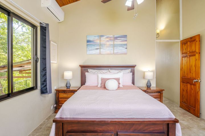 Cozy bedroom with wooden bed, two side tables, lamps, and ocean-themed artwork above the bed.