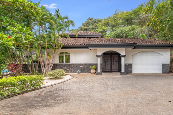 Modern house with tiled roof, arched entrance, and surrounding greenery.