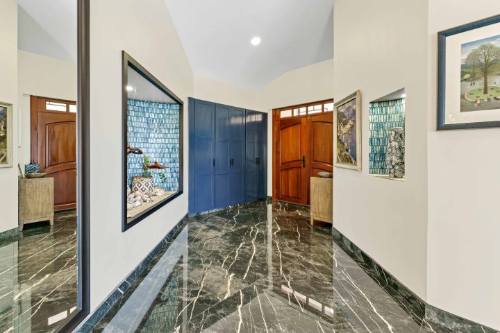 Luxurious hallway with marble floor, paintings, and wooden doors.