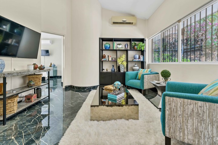 Modern living room with teal chairs, black shelves, glass table, and large window.