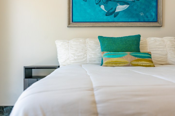 White bed with green pillows, a nightstand, and whale painting on the wall.