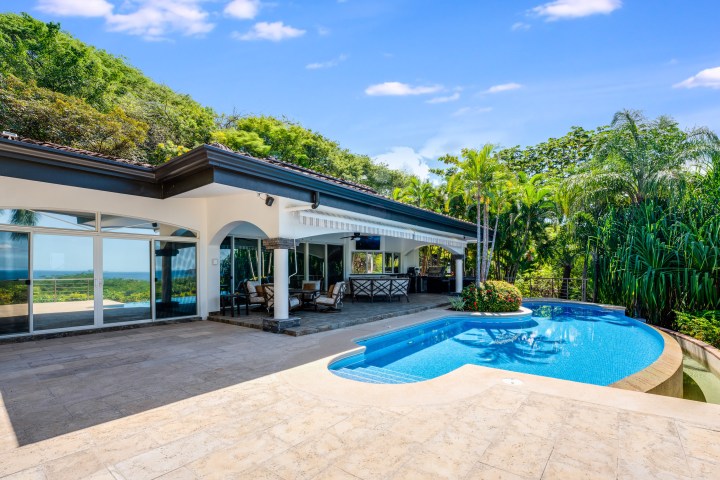 Luxurious villa with a pool, surrounded by tropical greenery and clear blue sky.