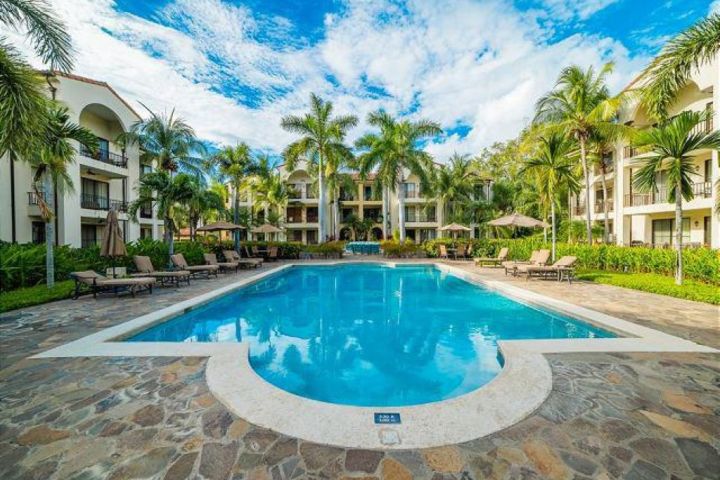 Outdoor pool with lounge chairs and palm trees at a resort under a blue sky.