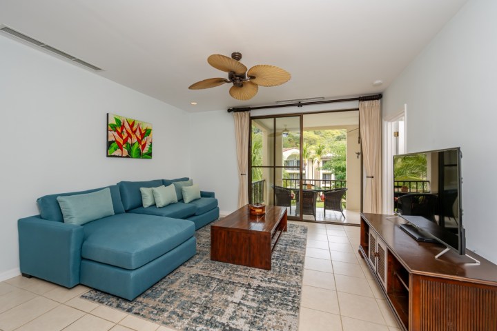 Living room with blue sectional sofa, wood table, TV, and balcony view.