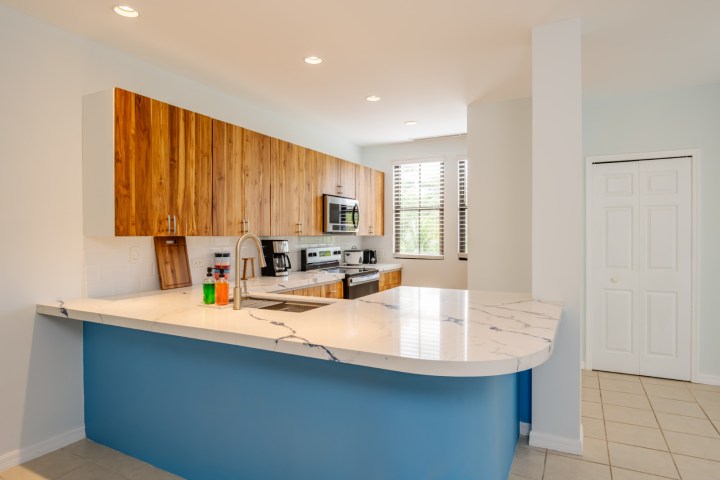 Modern kitchen with wood cabinets, marble countertop, and blue accent wall.