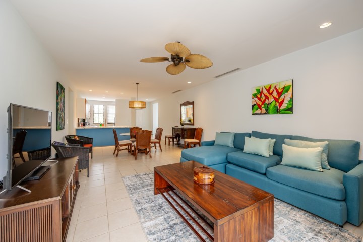 Living room with blue sofa, wooden coffee table, TV, ceiling fan, and dining area in the background.