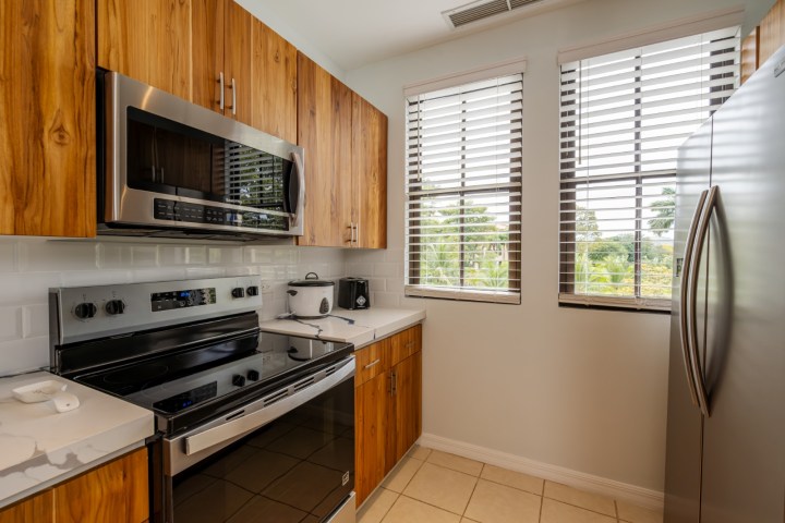 Kitchen with wooden cabinets, stainless steel appliances, and two windows with blinds.