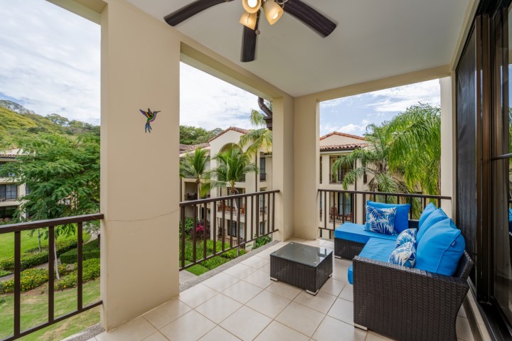 Balcony with blue cushioned seating, overlooking lush greenery and neighboring buildings.