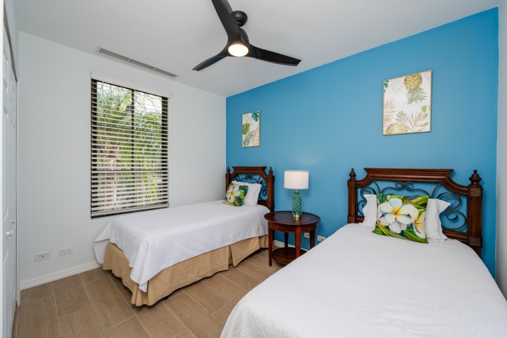 Bedroom with two single beds, blue accent wall, floral artwork, and a ceiling fan.