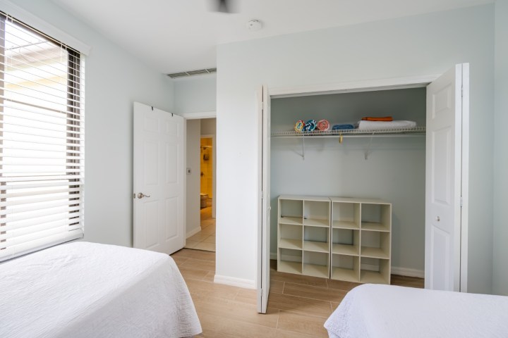 Bedroom with open closet, shelves, and two twin beds, next to a door leading to a bathroom.