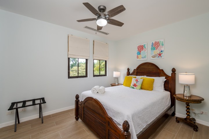 Cozy bedroom with a wooden bed, white bedding, ceiling fan, and wall art above the headboard.