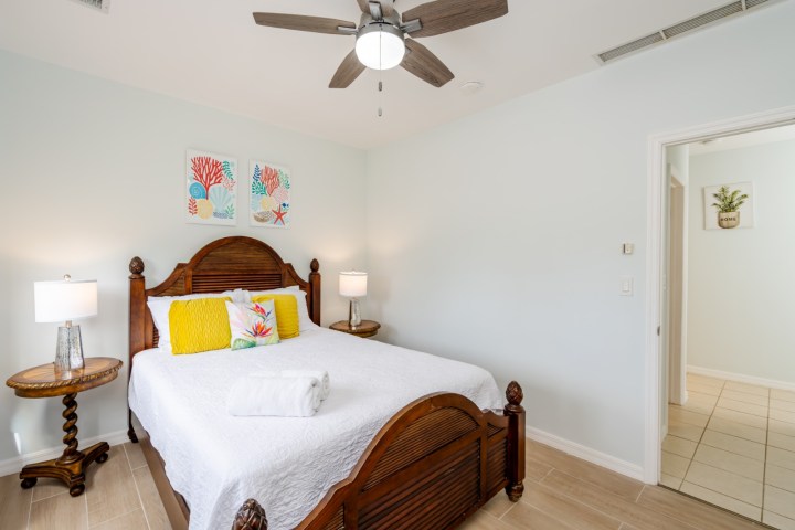 Bedroom with ceiling fan, wooden bed, colorful pillows, and two side tables with lamps.