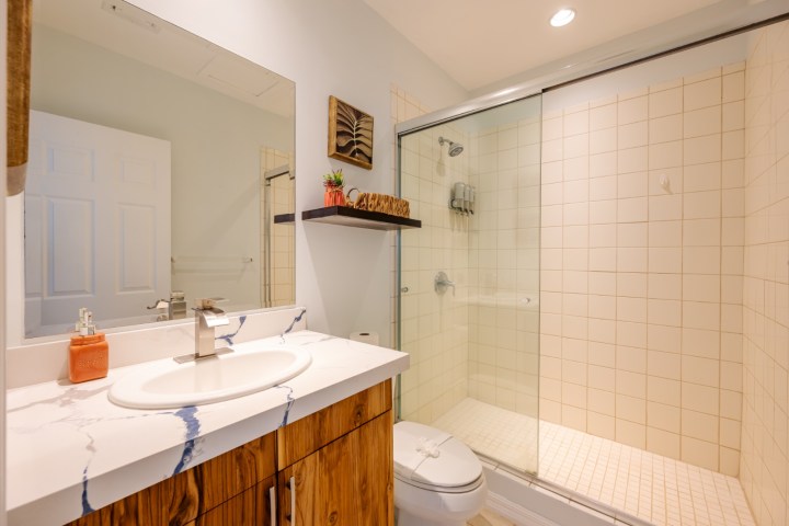 Modern bathroom with wood vanity, sink, large mirror, toilet, and tiled shower with glass door.
