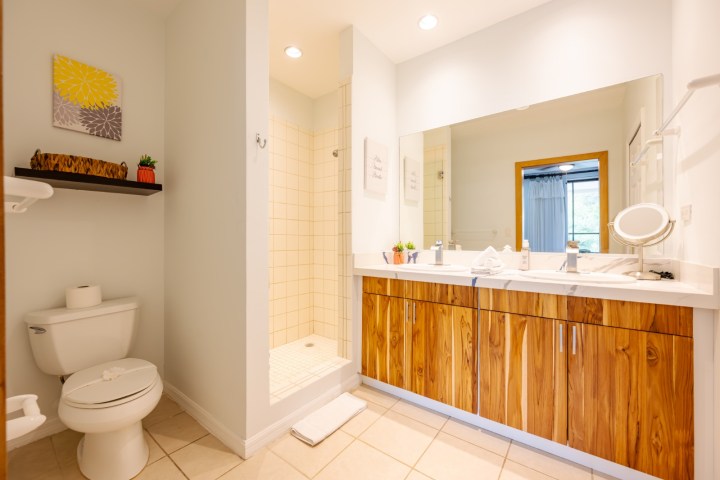 Bathroom with wooden vanity, large mirror, shower, toilet, and decor accents.
