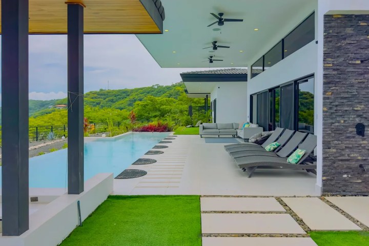 Outdoor patio with modern lounge chairs, pool, and lush green landscape view.