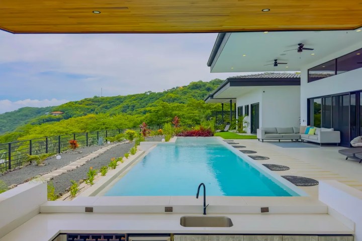 Modern patio with pool, outdoor seating, and lush green hillside view.
