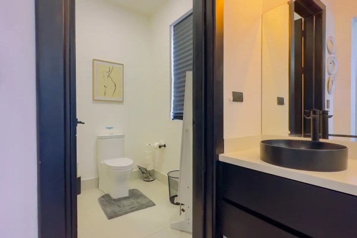 Modern bathroom with black sink, mirror, toilet, and wall art.