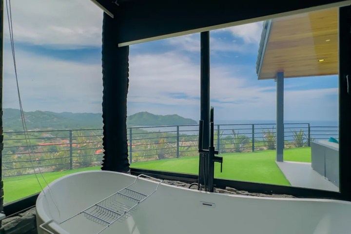 Modern bathroom with large window view of ocean and mountains.