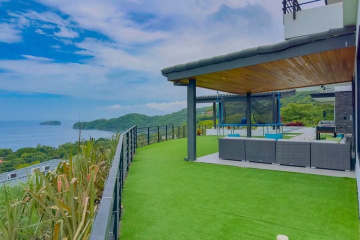 Modern terrace with view of ocean and hills, featuring seating area and lawn.