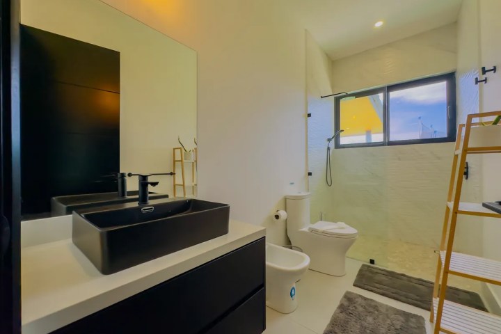 Modern bathroom with black sink, mirror, toilet, shower, and towel rack.