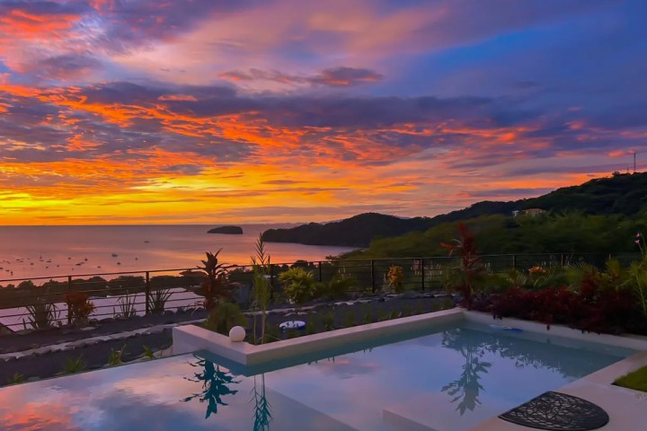 Sunset view of ocean and hills with a pool in the foreground.