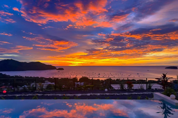 Vibrant sunset over ocean with colorful sky reflected in a swimming pool.