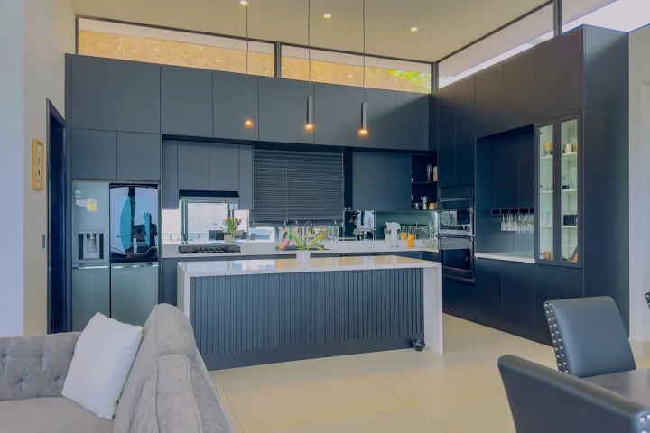 Modern kitchen with dark cabinets, large island, and hanging lights.