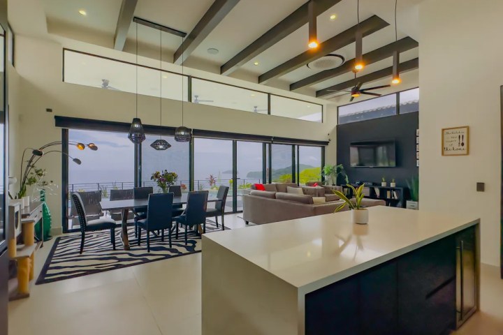 Modern open-concept living area with large windows, dining table, and sectional sofa facing the ocean view.