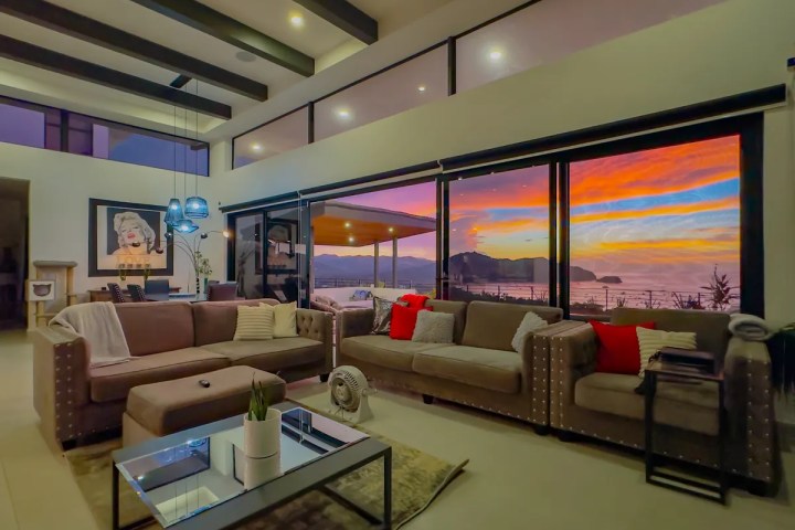Modern living room with sunset view through large windows, featuring two sofas and vivid sky colors.