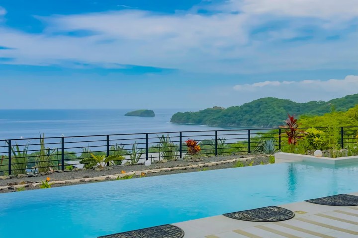 Infinity pool overlooking ocean and green islands under a blue sky.