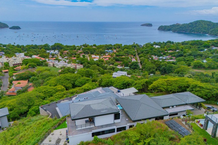 Aerial view of coastal town with houses and greenery near the ocean.