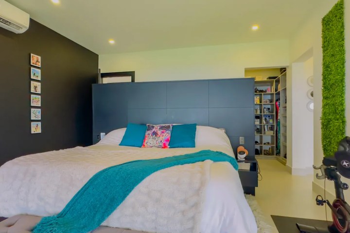 Modern bedroom with black accent wall, white bed, teal throw, and green wall art.