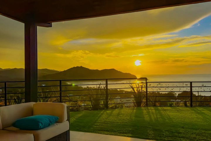 Patio with sofa overlooking ocean and mountains at sunset.