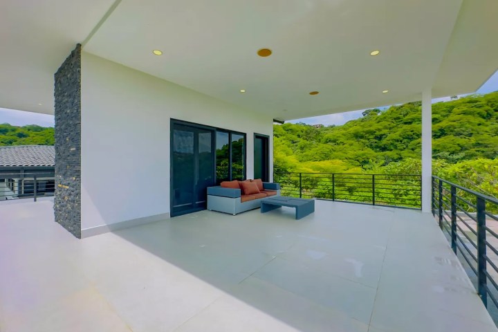 Spacious balcony with a sofa, table, and lush green view.