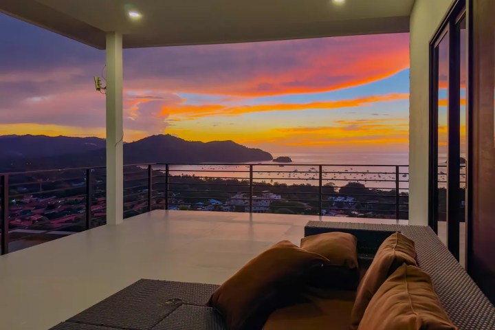 Modern patio with couches overlooking a sunset over hills and water.