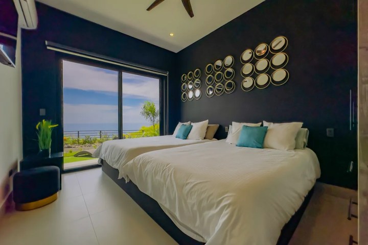 Modern bedroom with two beds, circular wall decor, sliding glass door, sea view.