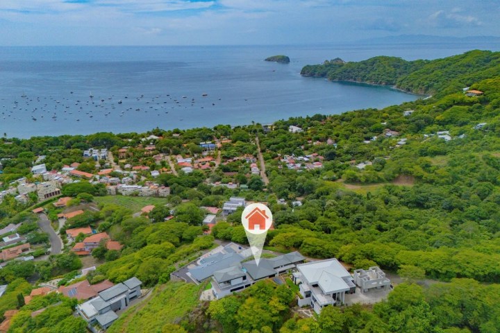 Aerial view of coastal town with lush greenery, ocean, and island in the background.