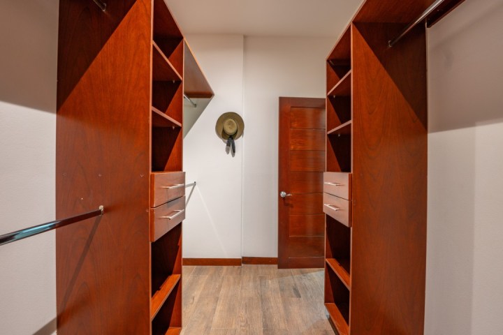 Empty walk-in closet with wooden shelves, drawers, and a hanging hat on the wall.